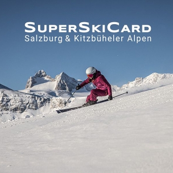 „Eine Skifahrerin in pinkem Skianzug und weißem Helm fährt in hoher Geschwindigkeit einen breiten, sonnigen Hang hinunter. Im Hintergrund ragen schneebedeckte Gipfel der Alpen vor blauem Himmel auf. Im oberen Bildbereich steht in großer, weißer Schrift ‚SuperSkiCard‘, darunter ‚Salzburg & Kitzbüheler Alpen‘.“