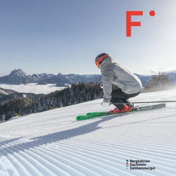 „Skifahrer in Hocke fährt eine frisch präparierte, geriffelte Skipiste hinunter. Im Hintergrund sind bewaldete Hänge, dahinter ein Nebelmeer und dahinter schroffe Gebirgsgipfel zu sehen. Oben rechts steht ein rotes ‚F‘ als grafisches Element, unten rechts der Schriftzug ‚Bergbahnen Dachstein Salzkammergut‘ mit drei farbigen Punkten.“