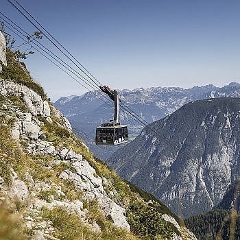 A cable car over a rocky mountain landscape with mountains in the background and a clear sky